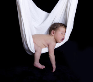 baby sleeping in white hammock swing against black background